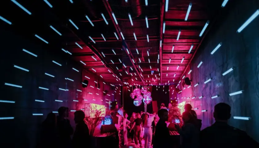 Ein **Partyraum gestalten** mit Neonröhren und Discokugeln. Menschen tanzen im pulsierenden Licht.