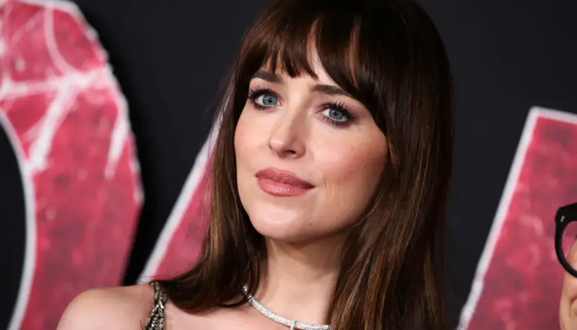 Dakota Johnson con un flequillo abierto y ojos azules intensos, luciendo un collar de diamantes.