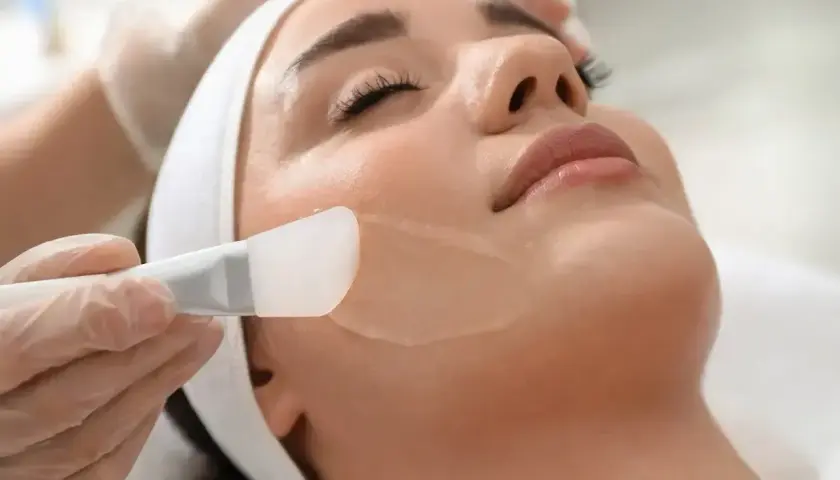 Kosmetyczka aplikuje żelowy peeling na twarz klientki. To pierwszy krok do gładkiej skóry.
