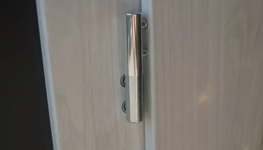 Metalowy zawias na jasnych drzwiach. Dowiedz się, jak podnieść drzwi na zawiasach, by je wyregulować lub zdjąć.