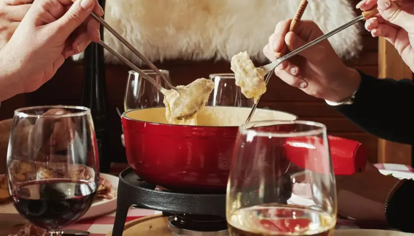 Des mains plongent des morceaux de pain dans une fondue pyrénéenne crémeuse, un moment convivial autour d'un plat réconfortant.