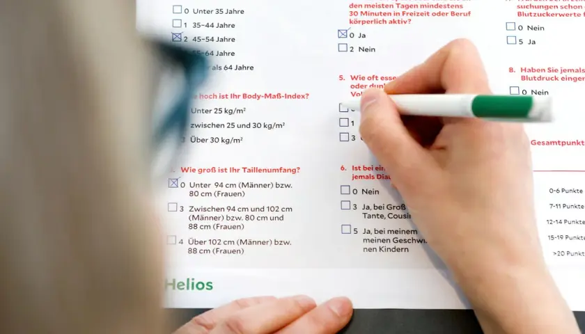 Hand füllt Fragebogen aus, der Fragen zu Lebensstil und Risikofaktoren für Diabetes enthält. Eine Diabetes Blutwerte Tabelle ist Teil des Dokuments.