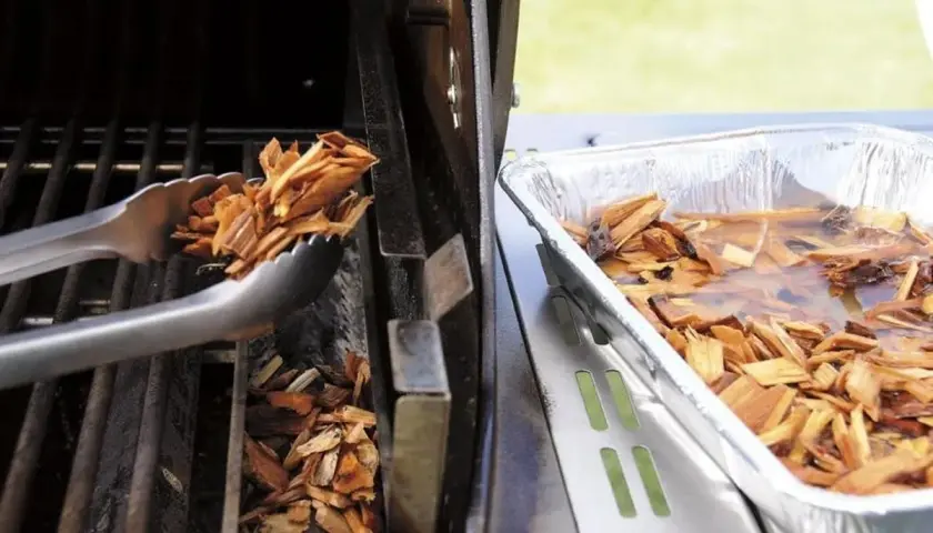 Des copeaux de bois sont placés dans un fumoir pour barbecue Weber. Une autre partie est trempée dans l'eau.