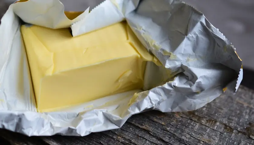 Kostka masła w folii aluminiowej na drewnianym blacie. Zastanawiasz się, czy można jeść przeterminowane masło?