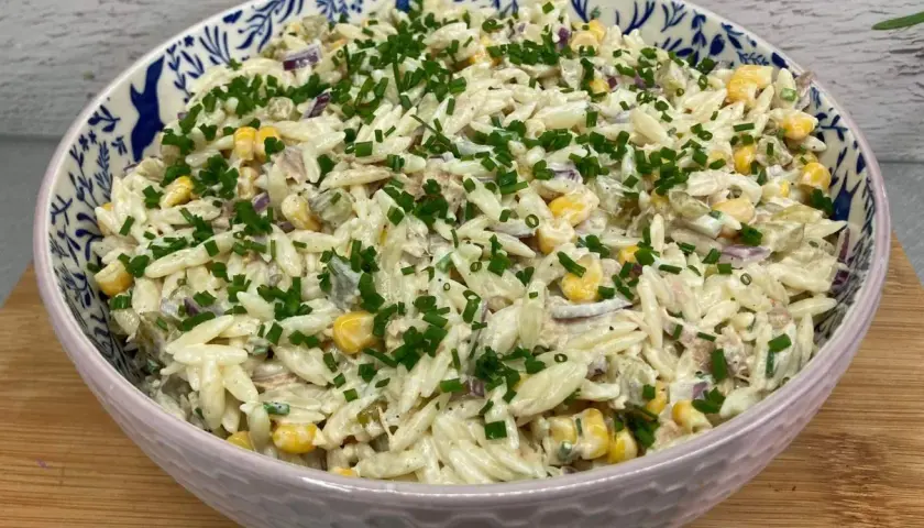 Pyszna sałatka z tuńczykiem i makaronem orzo, z kukurydzą i szczypiorkiem, w ozdobnej misce.