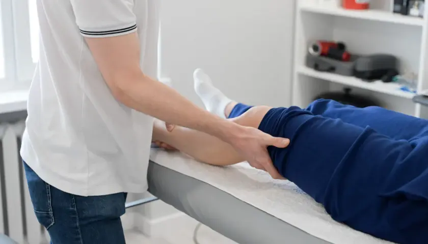Fizjoterapeuta wykonuje masaż nogi pacjenta leżącego na kozetce.