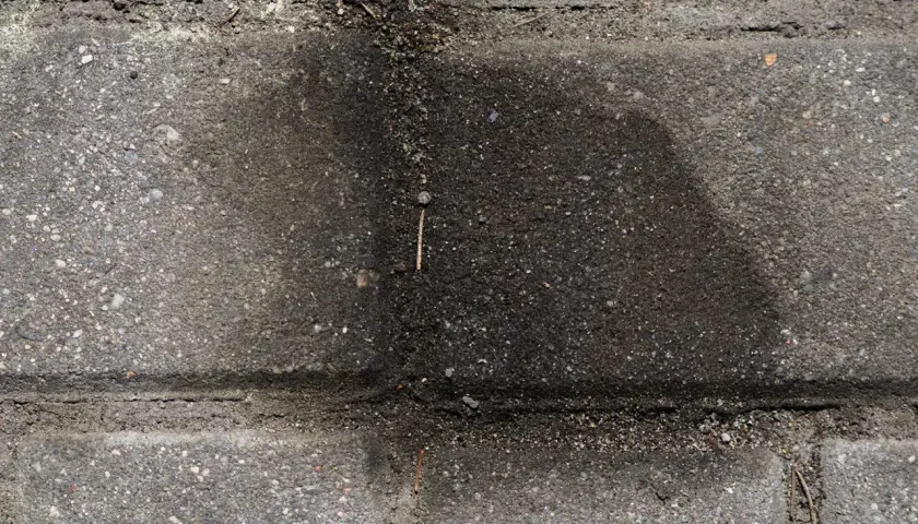 Stare plamy z oleju na kostce brukowej tworzą ciemny, rozlany kształt, świadcząc o dawnych wyciekach.