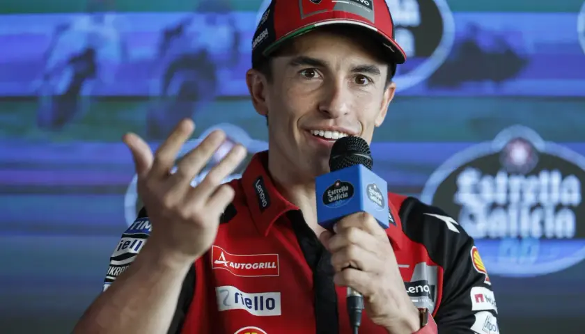 Marc Márquez, con su gorra roja y polo de Ducati, habla con un micrófono. Su edad se refleja en su energía y sonrisa.