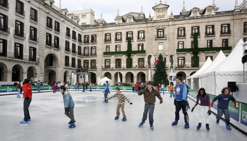 Gente patinando en la pista de hielo de Santander, con un árbol de Navidad y edificios históricos de fondo.