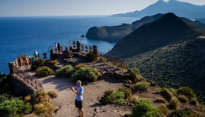Un hombre toma una foto en un mirador con vistas a la cala de enmedio y montañas.