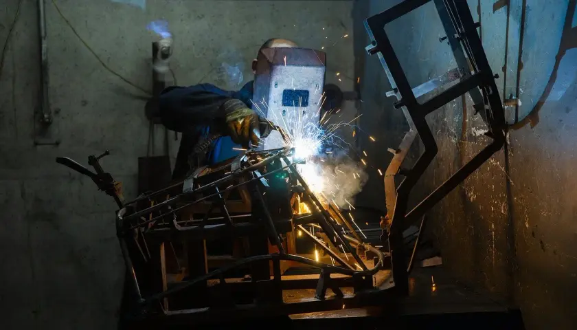 Spawacz w masce tworzy konstrukcję, iskry sypią się wokół. Czy to spawanie aluminium AC czy DC?