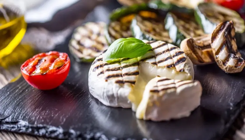 Kremowy camembert z grilla z pomidorkiem i warzywami na czarnej desce.