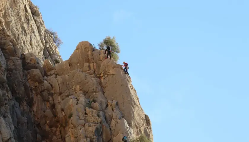 Tres escaladores desafían el chorro escalada en una pared rocosa bajo un cielo azul.