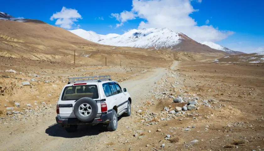Biały SUV na drodze gruntowej, w tle góry pokryte śniegiem. Przygoda na Pamir Highway.