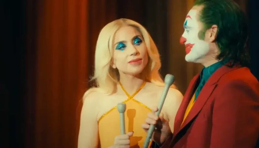 La femme du Joker, avec son maquillage bleu scintillant, semble chanter face à lui, le clown au visage blanc et rouge.