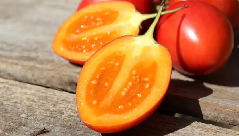 Tomates de palo rojos y brillantes, uno cortado por la mitad revelando su pulpa anaranjada y semillas.