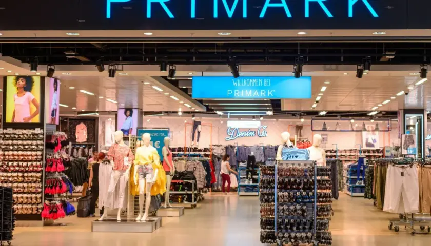 Wejście do sklepu Primark w Polsce. Widać neonowy napis "PRIMARK" i wystawione ubrania na manekinach i wieszakach.