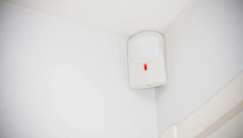 Detector de presencia blanco en esquina de pared, con luz roja encendida. Así es como funciona un detector de presencia.