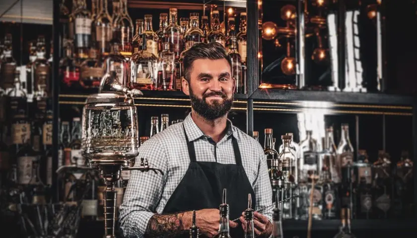 Barman z tatuażami prezentuje akcesoria do przygotowania absyntu. Poznaj tajniki, jak pić absynt, by w pełni docenić jego smak.
