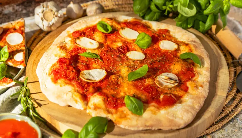 Eine köstliche Pizza Marinara mit Tomatensauce, Knoblauchscheiben und frischem Basilikum auf einem Holzbrett.