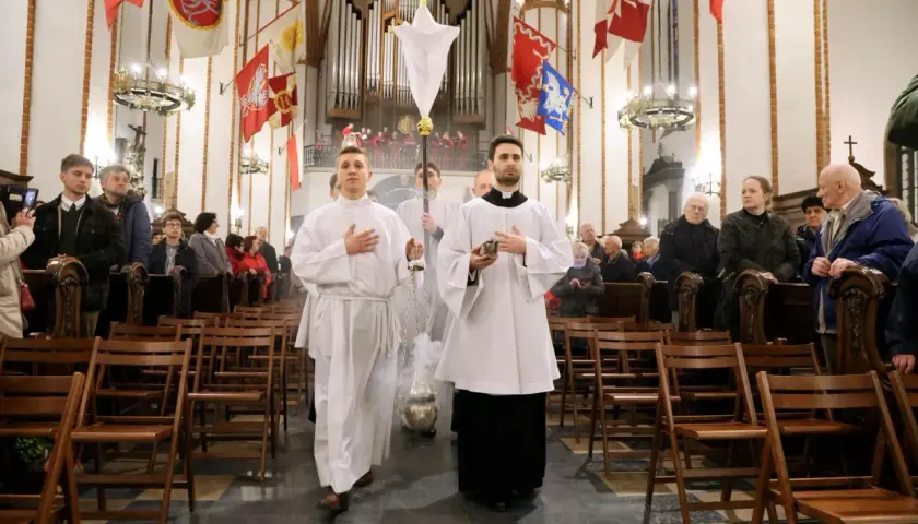 Liturgia Wielkiego Czwartku w kościele. Dwóch ministrantów w białych szatach niesie kadzidło i chorągiew.