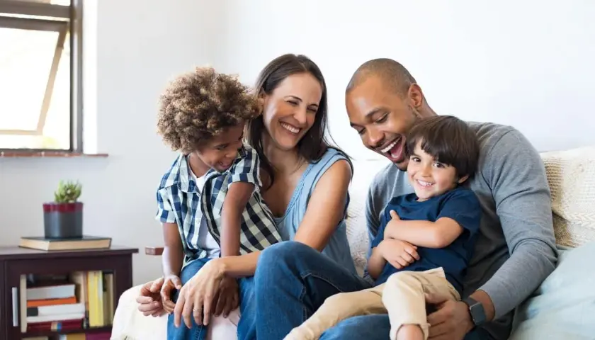 Famille souriante sur un canapé, profitant d'un moment de joie. Ce bonheur est rendu possible grâce à un **prêt conventionné** qui leur a permis d'acquérir leur foyer.