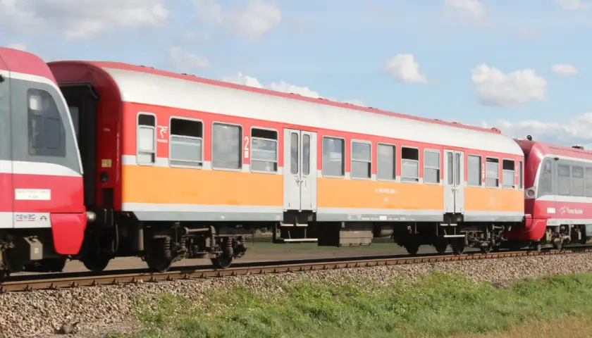 Lekki wagon pasażerski w kolorach pomarańczowo-białym i czerwonym jedzie po torach.