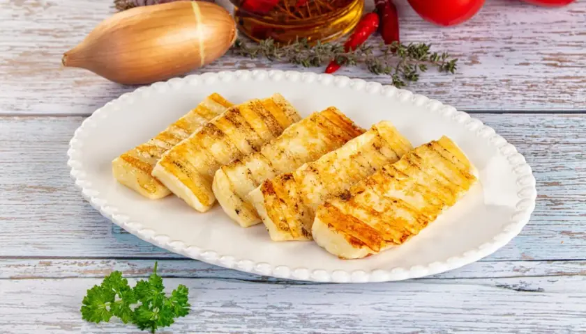 Grillowany ser halloumi na talerzu, idealny do prostych przepisów. W tle czosnek, chili i pomidory.