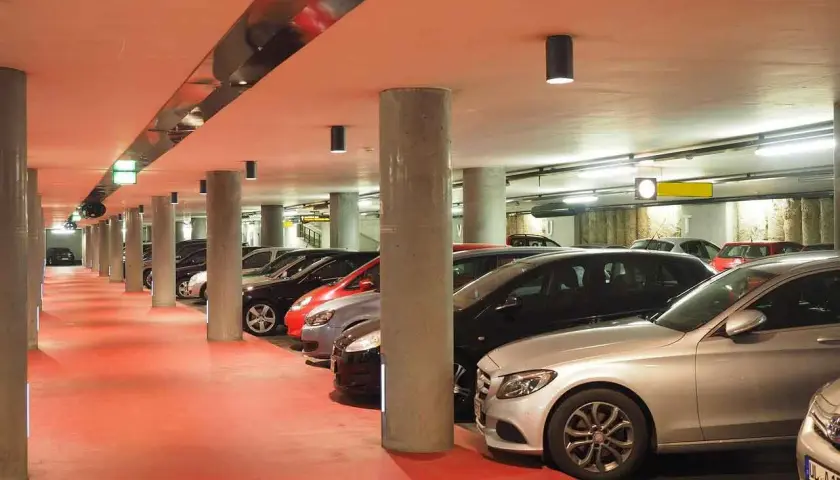 Intérieur d'un parking souterrain avec des voitures garées, sol rouge vif, éclairage artificiel. Un parking pratique pour explorer Venise.