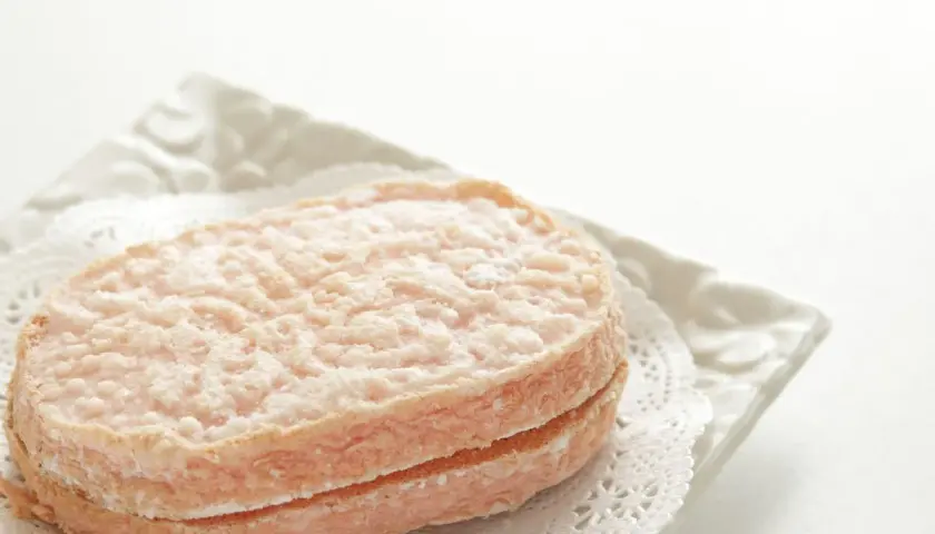 Delicato dacquoise alle nocciole, un dolce leggero e friabile, servito su un piatto bianco con un centrino di pizzo.