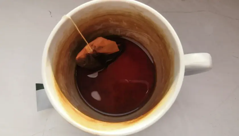 W kubku herbata z widocznym osadem na ściankach. Torebka z herbatą pływa w ciemnym naparze.