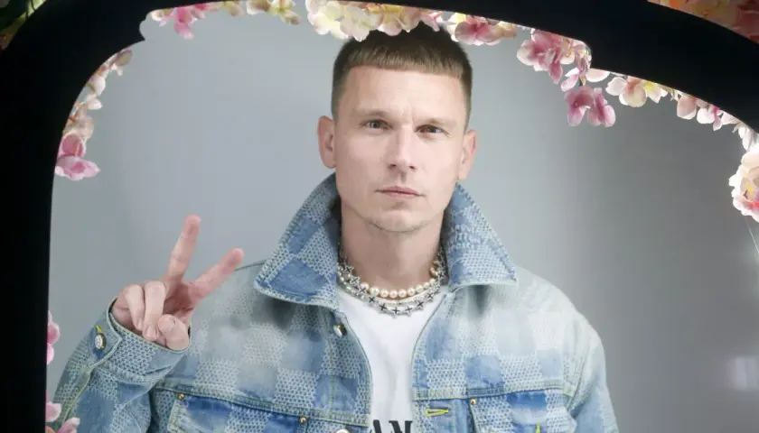 Bart Pniewski, młody mężczyzna w jeansowej kurtce, pozuje z uniesionym znakiem pokoju.