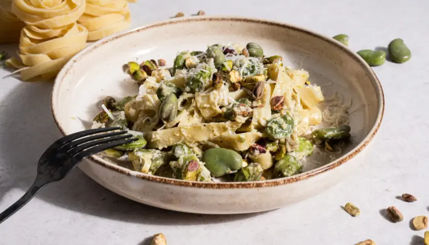 Makaron tagliatelle z bobem i pistacjami, posypany parmezanem, na talerzu.