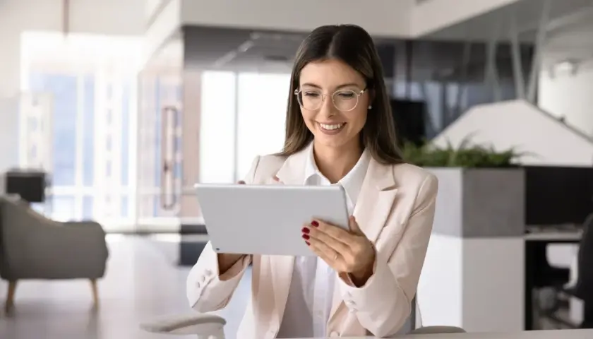 Uśmiechnięta kobieta w okularach przegląda tablet, zastanawiając się, czy umowa zlecenie wlicza się do stażu pracy.