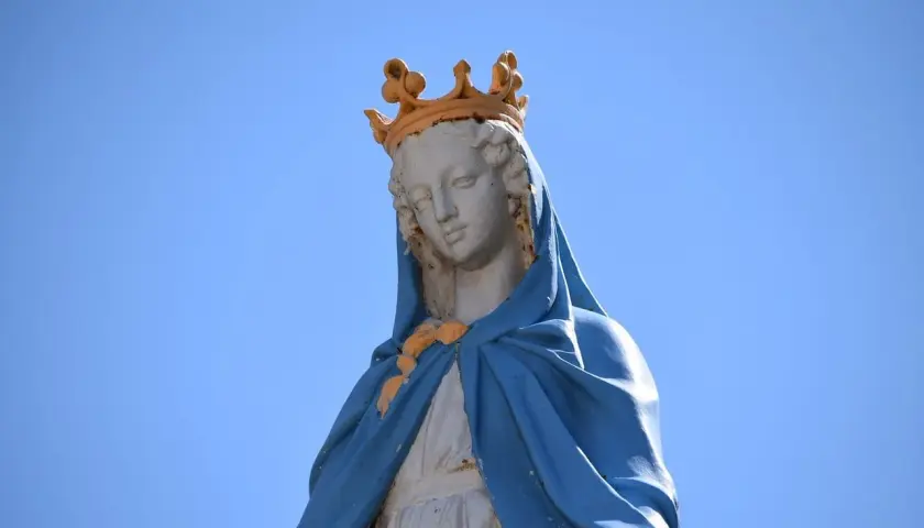 Figura Matki Bożej z koroną na głowie, w niebieskim płaszczu. Jej postawa przypomina błogosławieństwo z Psalmu 112.