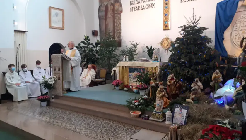Uroczystość w kościele z kapłanem przy pulpicie i szopką bożonarodzeniową. Święta Genowefa w centrum uwagi.