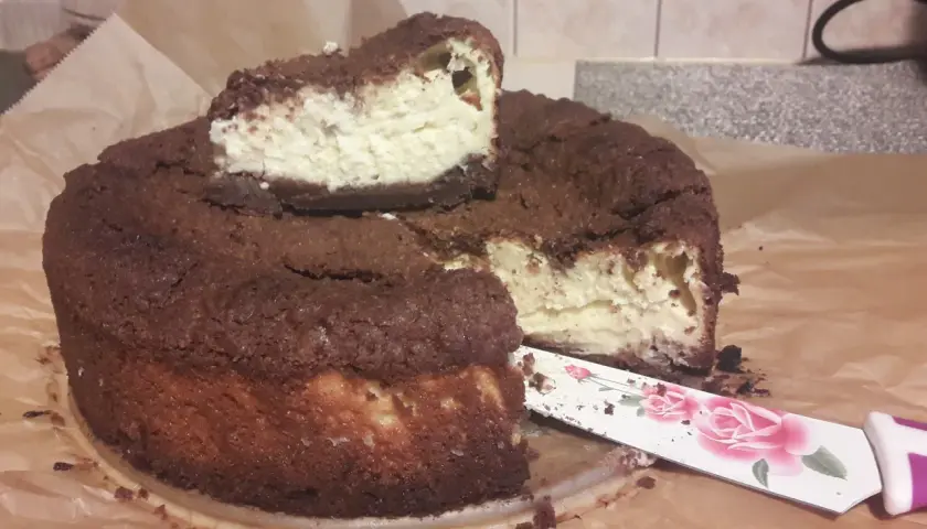 Pyszny sernik królewski bezglutenowy z czekoladową kruszonką i kremowym nadzieniem. Pokrojony kawałek czeka na spróbowanie.
