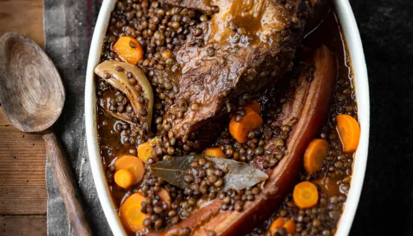 Un plat réconfortant de petit salé aux lentilles, avec des morceaux de viande savoureux, des carottes et des oignons, prêt à être servi.