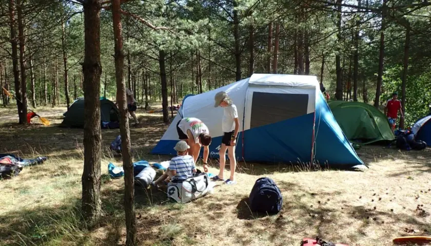 Rodzina rozbija obóz w lesie. Dzieci pomagają przy namiotach, zastanawiając się, jaki śpiwór na lato będzie najlepszy.