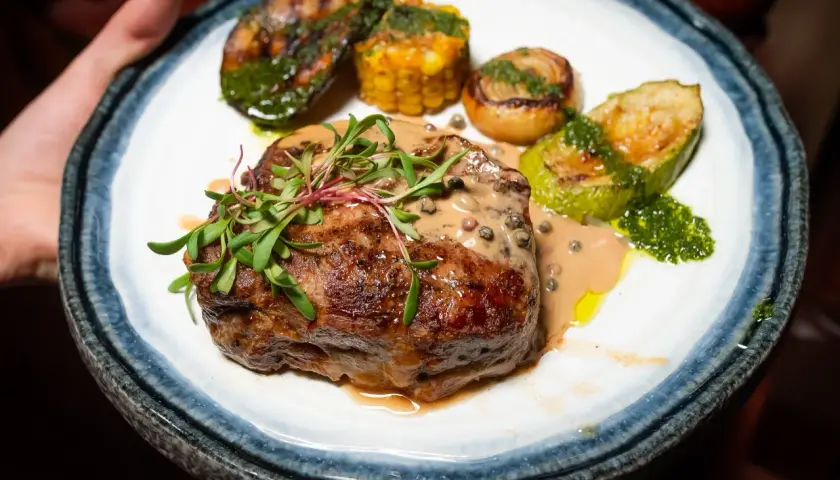 Un succulent filet mignon barbecue, nappé d'une sauce crémeuse aux poivres, accompagné de légumes grillés et de maïs.