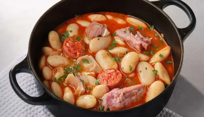 Judiones de la granja en cazuela negra, con chorizo, tocino y perejil picado. Un plato reconfortante y lleno de sabor.
