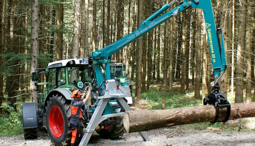 Ein Mann bedient den Kran eines Traktors im Wald. Das Schwenkwerk des Krans greift einen Baumstamm.