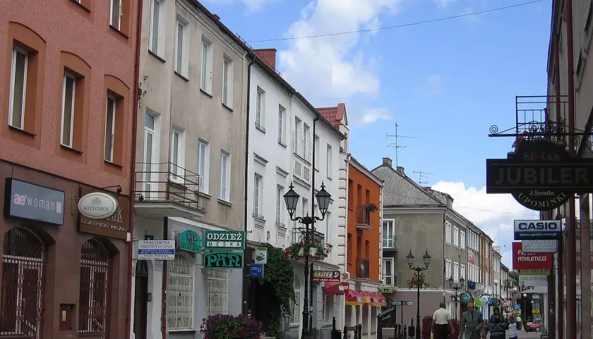 Ulica w Polsce, z kamienicami po obu stronach. Widać szyldy sklepów, m.in. "Jubiler" i "Casio". Kierunkowy 86 w Polsce.