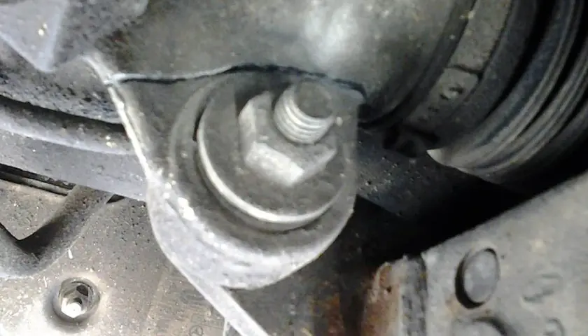 Soporte metálico con un perno hexagonal sujetando una pieza del motor, cerca de un componente que podría ser parte del volante de dirección.
