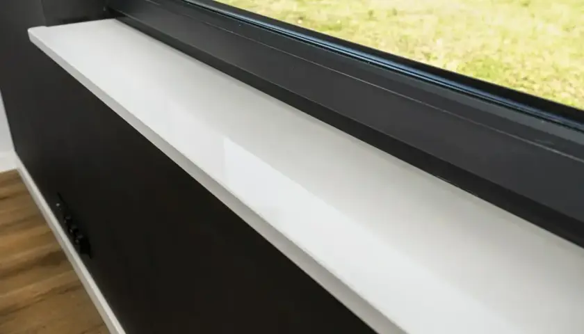 Jasny parapet z konglomeratu z widocznymi plamami, obok czarnej ściany i okna.