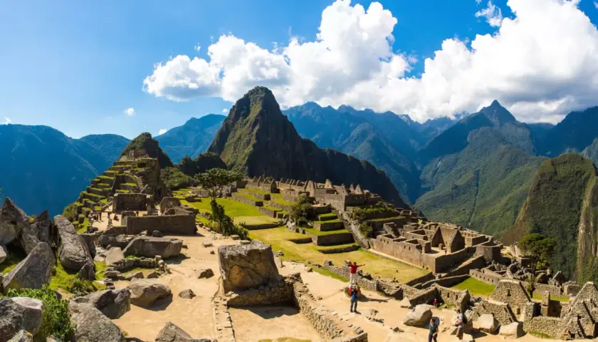 Machu Picchu, dawna twierdza Inków, wznosi się wśród zielonych gór. Turyści zwiedzają ruiny, podziwiając dzieło Inków.