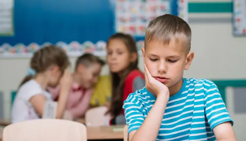 Un bambino solo in classe, con la mano sul viso, mentre altri bambini ridono e parlano tra loro. Sembra che mia figlia non abbia amici.