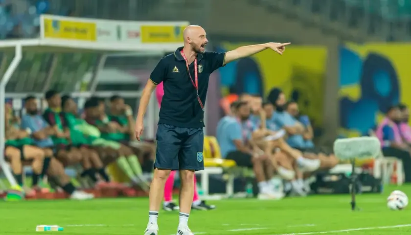 Tomasz Tchórz, trener, wskazuje kierunek na boisku. Za nim siedzą zawodnicy na ławce rezerwowych.