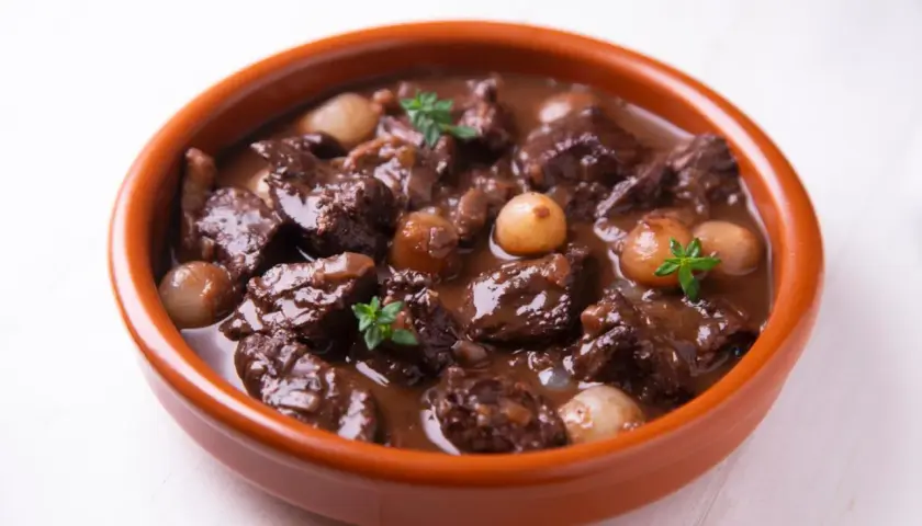 Herzhaftes Spezzatino di manzo mit kleinen Zwiebeln und Kräutern in einer Terrakotta-Schale.