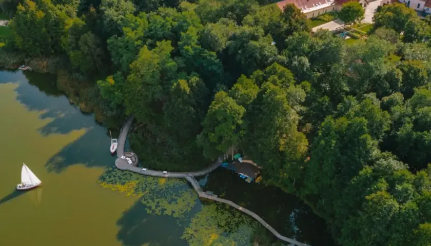 Widok z lotu ptaka na jezioro, które może być najczystsze w Polsce. Widać żaglówkę, pomost i otaczający las.